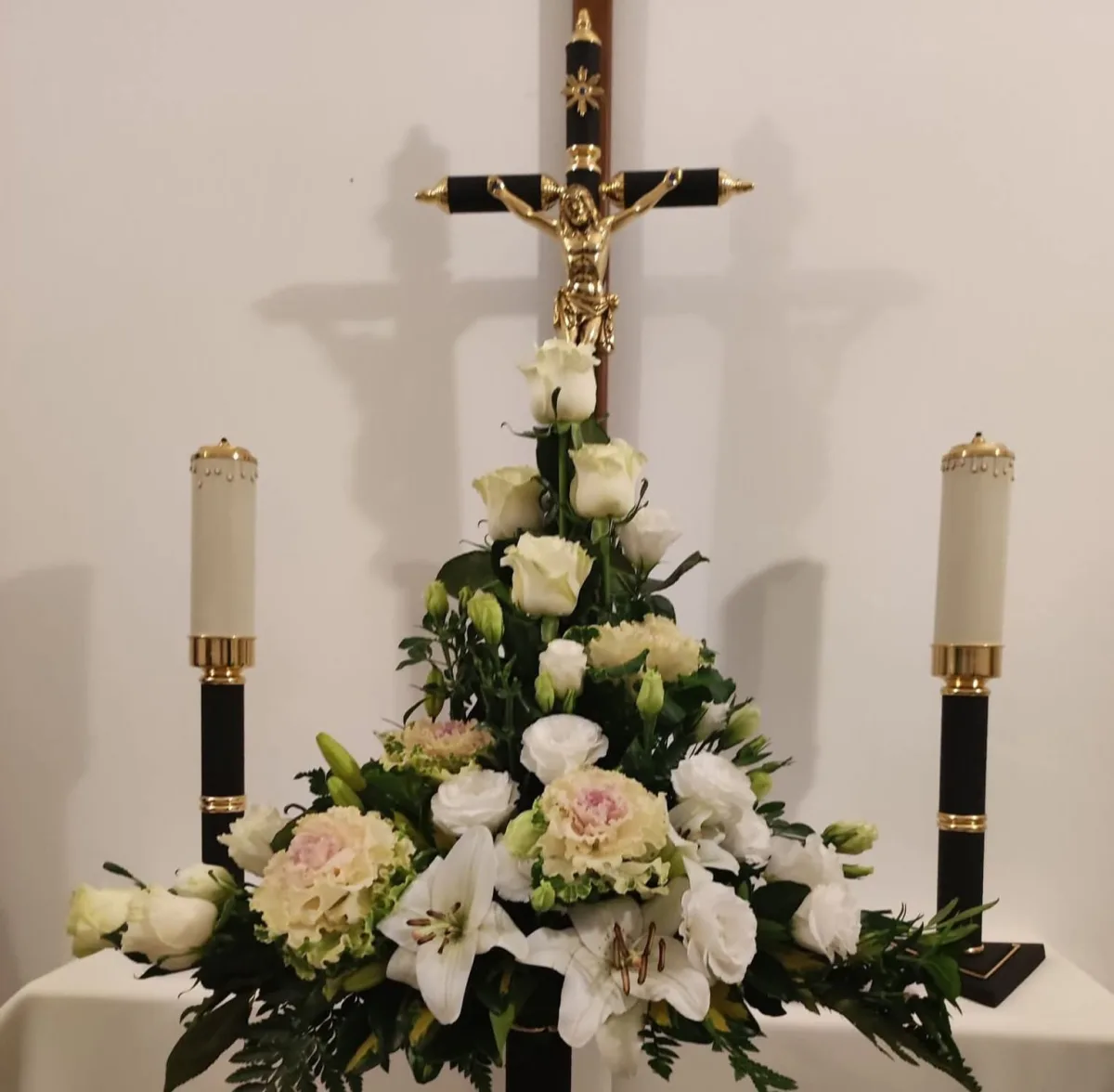 Arranjo floral junto a cruz e velas para cerimónia fúnebre